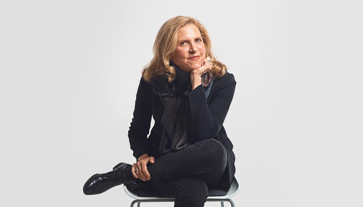 Cheerful woman sitting cross-legged on a chair engaged in conversation with you.