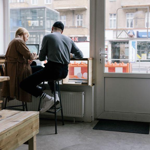 Man and woman on stools doing work things from what appears to be some sort of coffee shop.